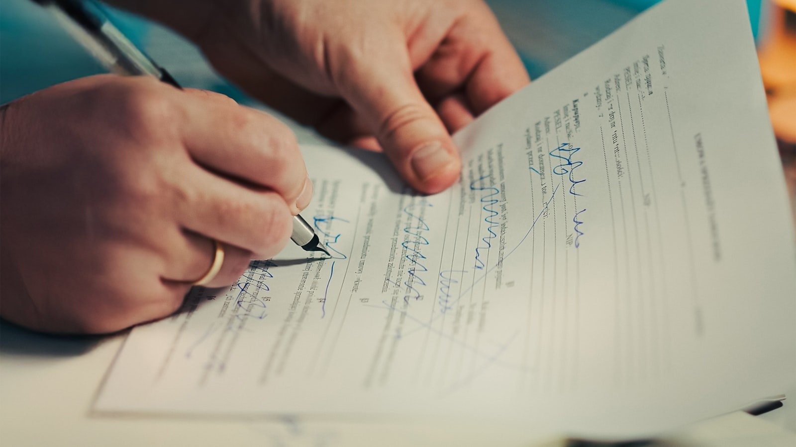 Close-up of hands signing a marked-up vehicle document with a pen